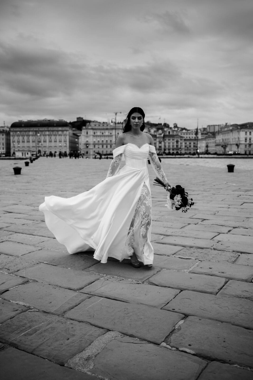 Bride walking across Molo Audace during a black and white wedding photoshoot with the Trieste waterfront in the background, Italy