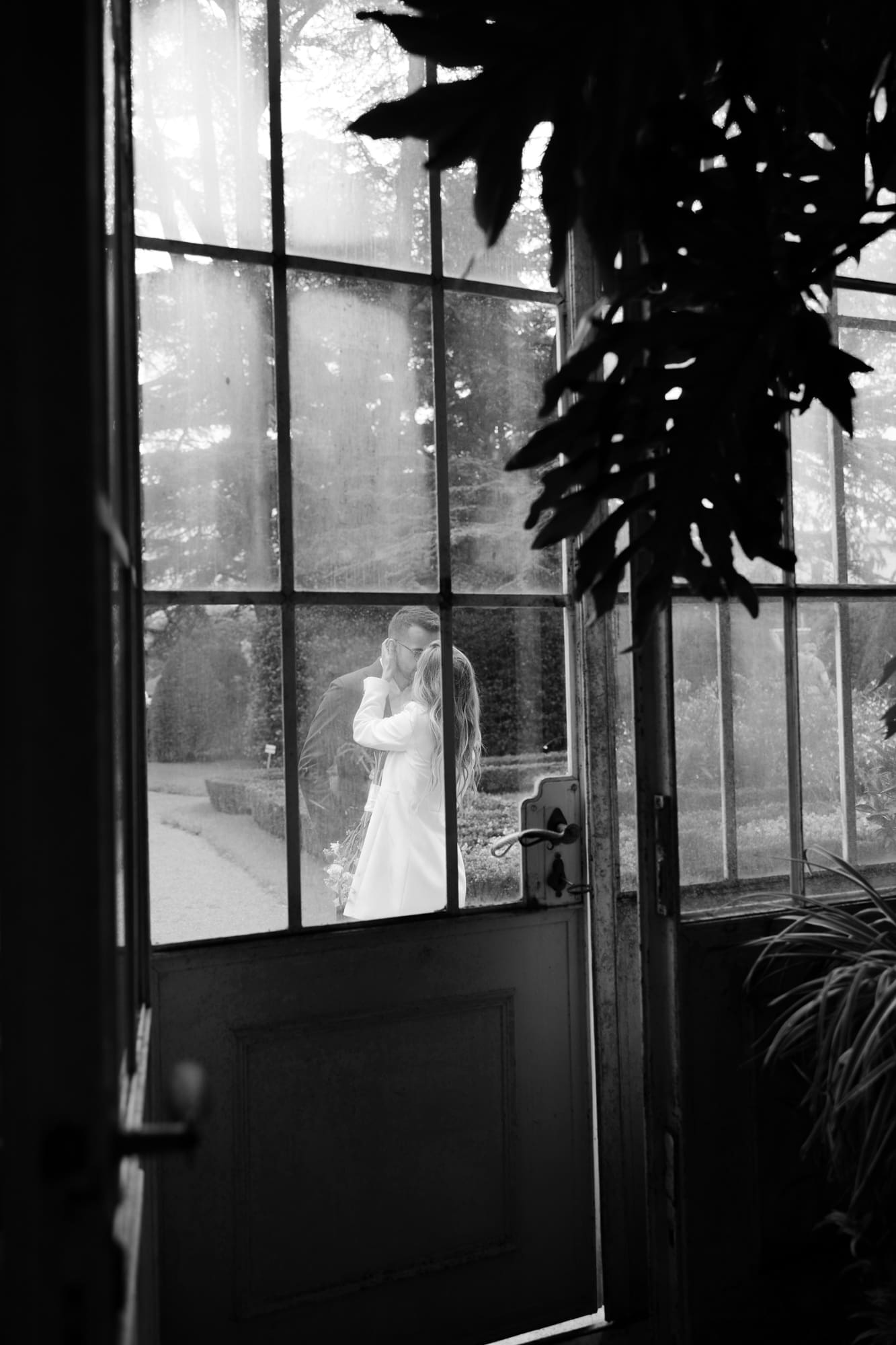 Bride and groom seen through the glass doors of the historic greenhouse at Villa Mirasasso in Slovenia.
