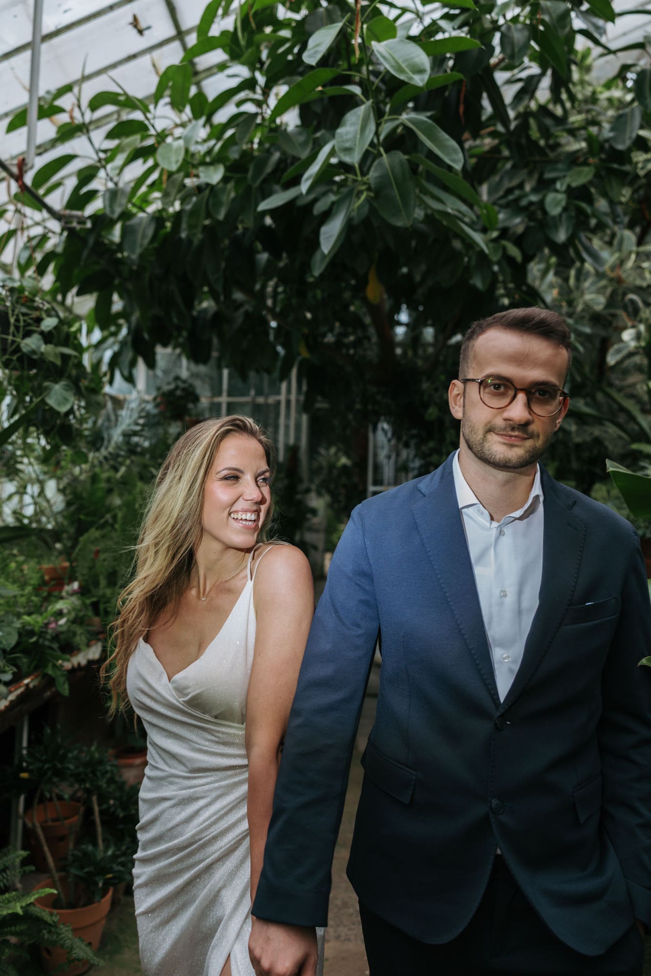 Newlyweds holding hands among exotic plants inside the historic greenhouse at Villa Mirasasso in Slovenia.
