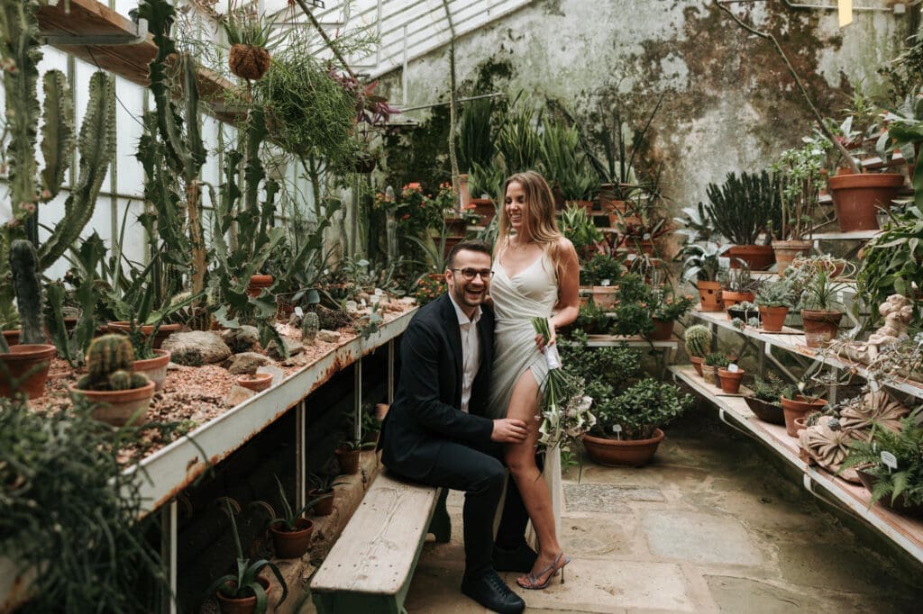 Bride and groom posing among cacti and exotic plants inside the historic greenhouse at Villa Mirasasso in Slovenia.