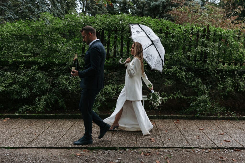 Bride and groom walking through the gardens of Villa Mirasasso under an umbrella on a rainy wedding day in Slovenia.