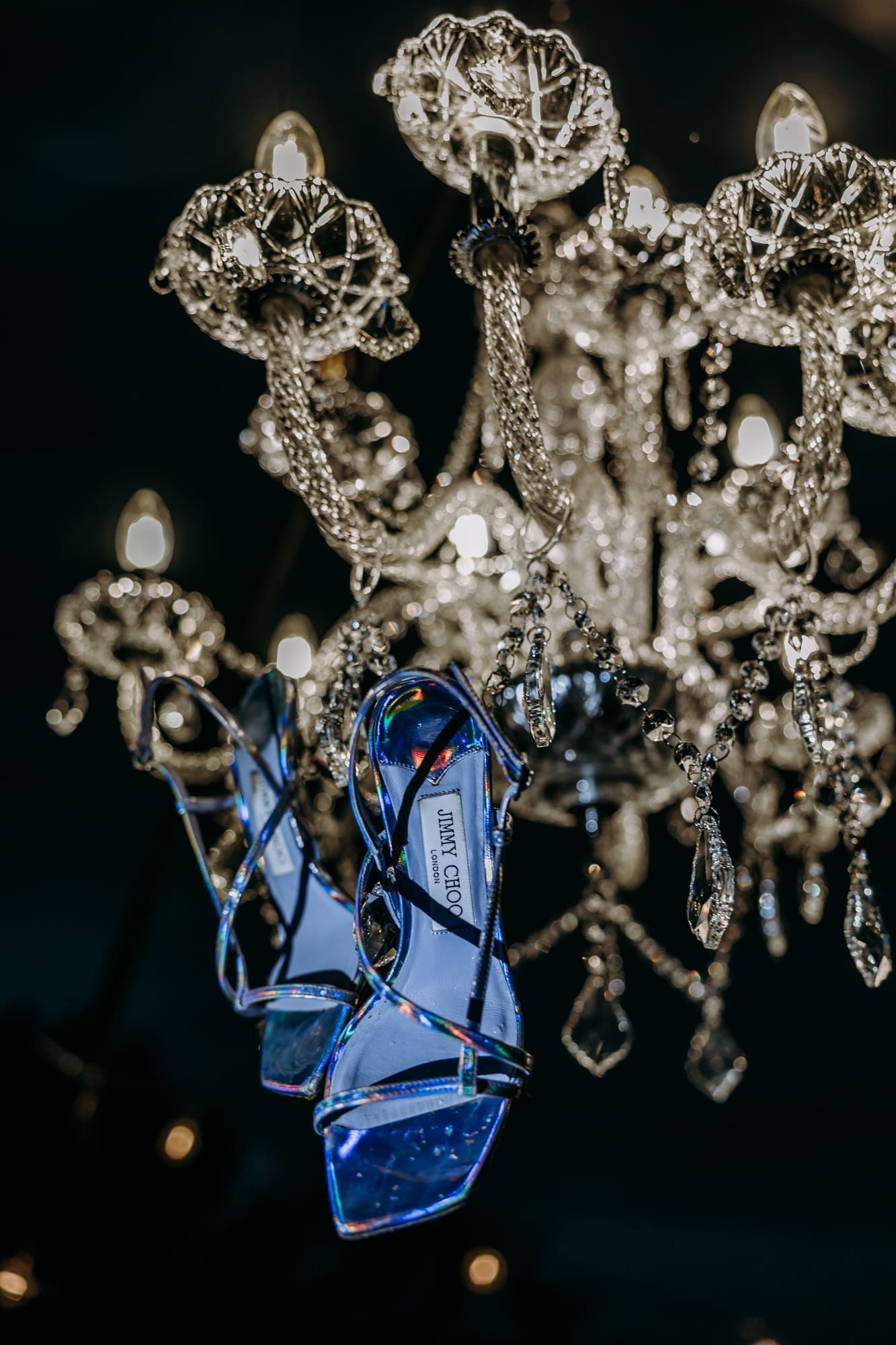 Bride's Jimmy Choo wedding heels hanging from a crystal chandelier during an intimate wedding celebration in Slovenia.