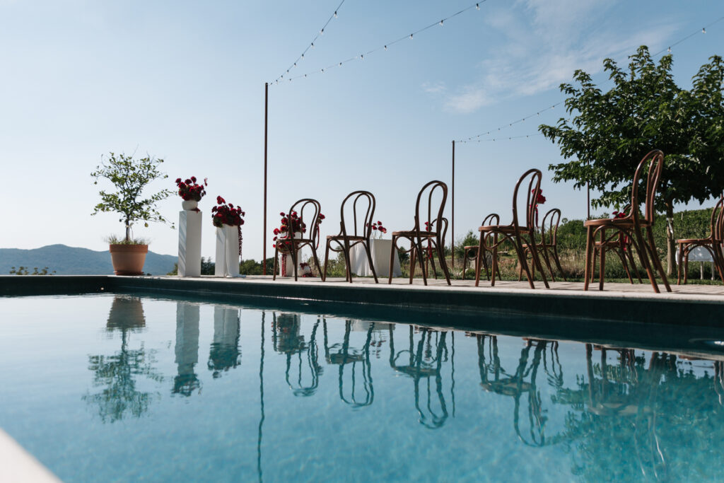 Wedding ceremony chairs and red floral arrangements reflected in the pool at Winery Škerlj in Slovenia’s Karst region.